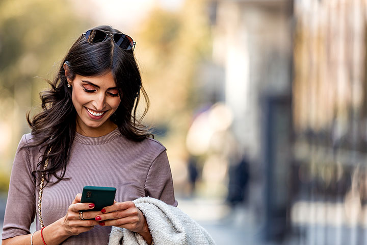 DigitalBanking_720x480 Woman on sidewalk looking at cell phone and smiling